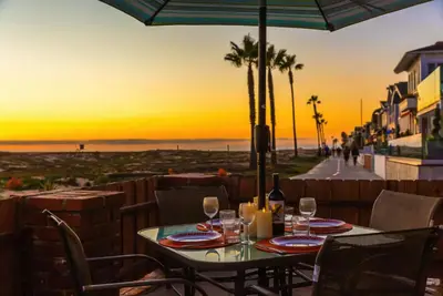 a table with wine glasses on a patio with a view of the beach at 5 Bedroom Duplex on the Boardwalk next to Balboa Pier in Newport Beach