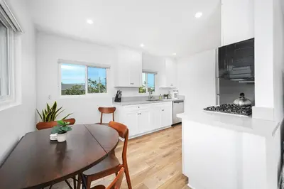 a white kitchen with a wooden table and a wooden floor at Remodeled - Modern - 2 Bedroom - Walk to the Beach in Newport Beach