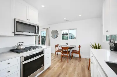 a kitchen with white cabinets and a table with chairs at Remodeled - Modern - 2 Bedroom - Walk to the Beach in Newport Beach