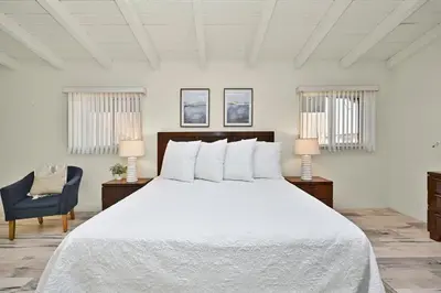 a bedroom with a white bed and a blue chair at Oceanfront Home on the Boardwalk with 3 car Garage, AC, Giant Patio, Ocean Views, Walk to Pier in Newport Beach