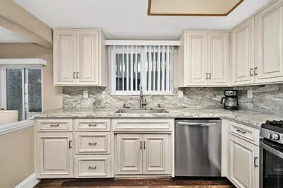 a kitchen with white cabinets and a stainless steel dishwasher at Giant Beachfront Home with Parking near the Pier in Newport Beach