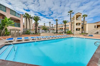 a swimming pool with lounge chairs and palm trees at Ocean-View Imperial Beach Condo with Community Perks in Imperial Beach
