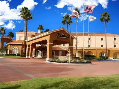 a building with two american flags and palm trees at Hotel San Diego-Rancho Bernardo in Rancho Bernardo