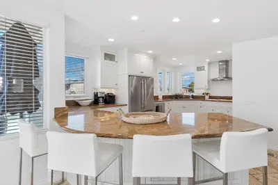 a kitchen with white cabinets and a island with white chairs at The Mission Beach VIP- 3 Decks, AC, Steps to Sand! in San Diego