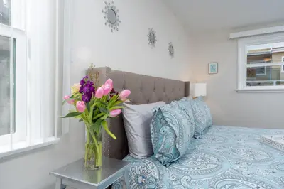 a vase of flowers on a table next to a bed at 100 PERCENT NEW STUNNING HUGE HOME, GARDEN BEACH, RESERVED Parking in Laguna Beach