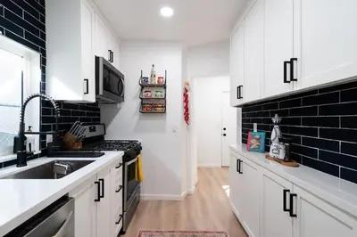 a kitchen with white cabinets and a black brick wall at * Bueno Bueno Casita * / 7 min to Downtown / 4 Bdr in San Diego