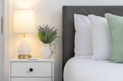a bed with a lamp and a vase with flowers on a night stand at 3 Bedroom House - Fire Pit Table BBQ - 10 Guests in La Mesa