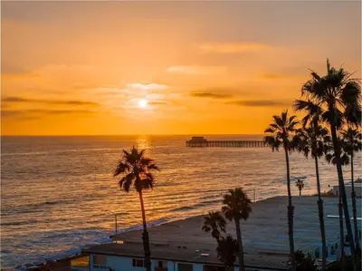a sunset over the ocean with palm trees and a pier at Amazing Place by the Sea - O'side Palms in Oceanside