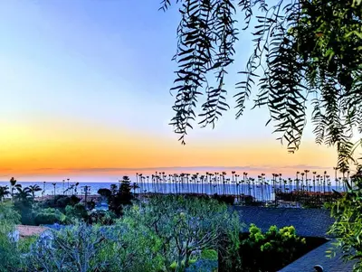 a sunset over a beach with trees and a fence at La Jolla Retreat in San Diego