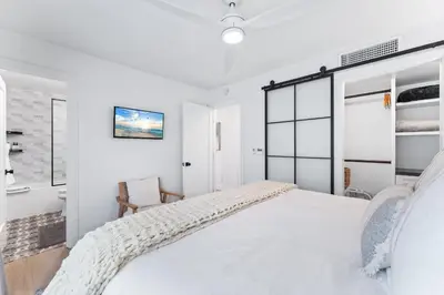 a white bedroom with a bed and a chair at Luxury Ground S Oceanfront Unit with Boardwalk Lounge Firepit - AC in San Diego