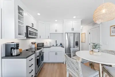 a kitchen with white cabinets and a table with chairs at Luxury Ground N Oceanfront Unit with Patio Lounge in San Diego