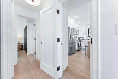 a hallway with white walls and a kitchen with a refrigerator at Luxury Ground N Oceanfront Unit with Patio Lounge in San Diego