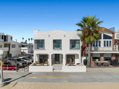 a white building with a palm tree in front of it at West Oceanfront Oasis 4 in Newport Beach