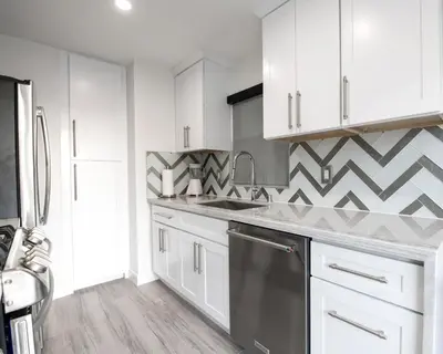 a kitchen with white cabinets and a geometric wall at Upper West Newport in Newport Beach