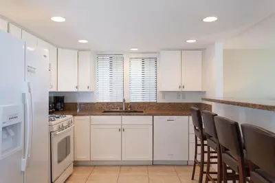 a kitchen with white cabinets and a sink and chairs at 3112 W Oceanfront A in Newport Beach