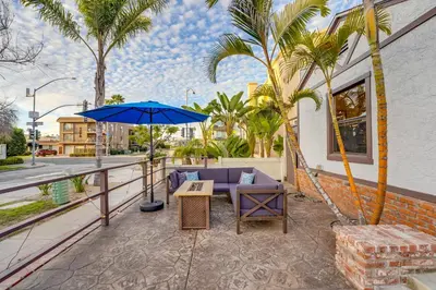a patio with a couch and an umbrella and palm trees at Sail Bay Dream - Steps to the bay! in San Diego