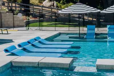 a swimming pool with blue chairs and an umbrella at Serene Outdoor Oasis Wine Country Home with Views in Glenoak Hills