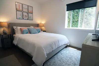 a bedroom with a bed with white sheets and blue pillows at La Jolla Beach Villa Gem in San Diego