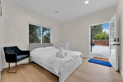 a white bedroom with a bed and a black chair at Urban Retreat Fun Relax Self Check-In Hot Tub Foosball Fire Pit Cornhole in The Woods Trailer Park