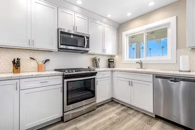 a kitchen with white cabinets and stainless steel appliances at Stunning 2nd Floor Beachfront Home with Balcony, Ocean Views, and Prime Location in Newport Beach