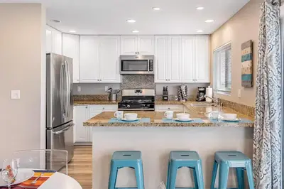 a kitchen with white cabinets and blue stools at Oceanfront Oasis in Newport Beach Steps to Balboa Park, Pier, and The Fun Zone! in Newport Beach