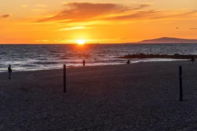 a sunset on a beach with people in the water at Oceanfront 3BR Home with Pool Table & Patio in Newport Beach