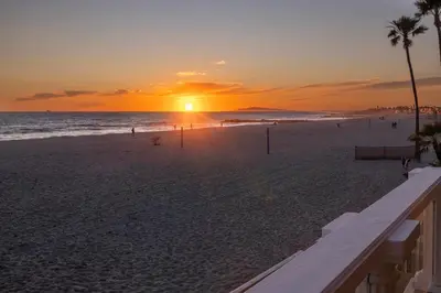 a sunset on a beach with palm trees and the ocean at Spacious 5BR Beach Home with Ocean Views in Newport Beach