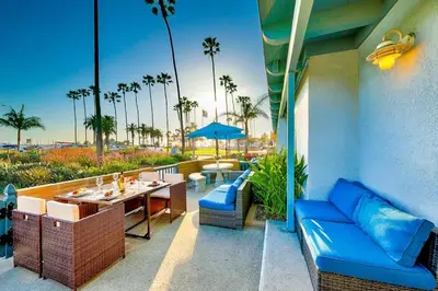 a patio with a table and blue furniture and palm trees at Newport Beach Condo with Patio Perfect Location on the Boardwalk in Newport Beach
