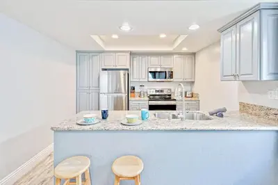 a kitchen with white cabinets and a counter with two stools at Balboa Peninsula Hidden Gem with Private Balcony & Stunning Views in Newport Beach