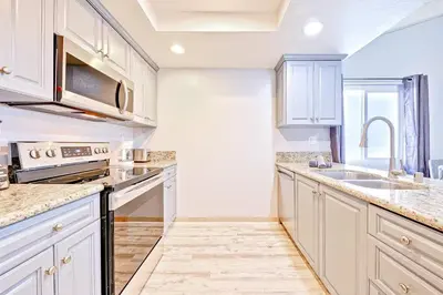 a kitchen with white cabinets and a sink at Balboa Peninsula Hidden Gem with Private Balcony & Stunning Views in Newport Beach