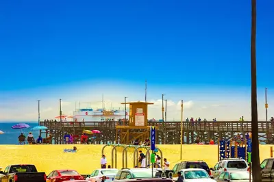 a beach with a pier and cars parked on the sand at Oceanfront Condo in Newport Beach with Private Balcony and Perfect Location by the Pier in Newport Beach