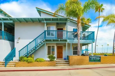a white house with blue balconies and a palm tree at Oceanfront Condo in Newport Beach with Private Balcony and Perfect Location by the Pier in Newport Beach