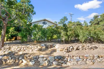 a stone wall in front of a house with trees at Julian Cafe Cottages With Breakfast At The Julian Cafe in Julian