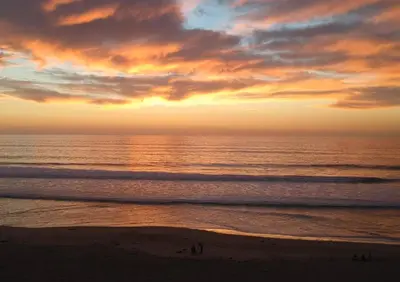 a sunset over the ocean with people walking on the beach at Ocean, Bay, Downtown, and City view Condo, Few steps from the ocean in San Diego