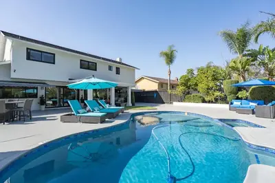 a swimming pool with chairs and umbrellas next to a house at Designer Family Home with Resort-Style Oasis in San Diego