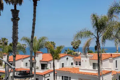 a group of palm trees and buildings with the ocean in the background at Nantucket-Style - Steps to Beach Rooftop Deck Ocean Views in San Diego