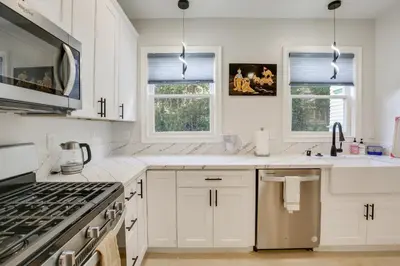 a white kitchen with white cabinets and windows at Steps to Balboa Park Sunny Historic Apartment in San Diego