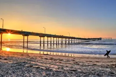 a person walking on the beach near a pier at PB 1BR BOHO with Parking, AC, and Large Patio in San Diego