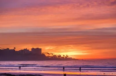 a sunset over a beach with people standing in the ocean at The Shores 7 in San Diego