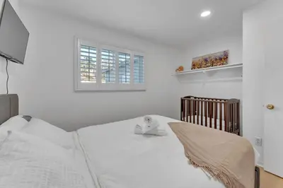 a white bedroom with a bed and a crib at Hilltop Home Hot Tub BBQ Game Room Self Check-In in Poway