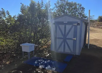 a blue outhouse with a door next to some trees at A Cozy Fireside Glamping Escape with Ridge Views in Fallbrook