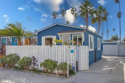 a blue house with a white fence and palm trees at Surf Cottage 2 in San Diego