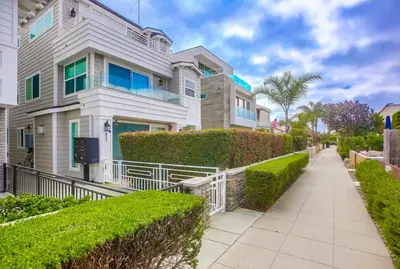 a white house with green bushes and a sidewalk at Pacific Pearl in San Diego