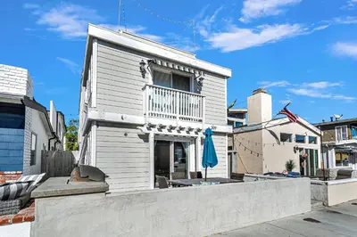 a white house with a balcony and an umbrella at Beach Escape with Patio! 2 Min Walk to Sand & Surf in Newport Beach