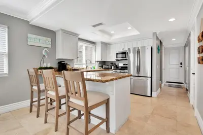a kitchen with white cabinets and a counter with chairs at Beach Escape with Patio! 2 Min Walk to Sand & Surf in Newport Beach
