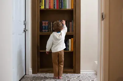 a young child standing in front of a book shelf at 5BR Oasis with Pool, Arcade, Sauna in La Mesa