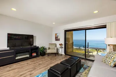 a living room with a tv and a large window at Oceanfront Sea'batical - SBTC212 in Solana Beach