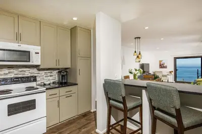 a kitchen with white appliances and a counter with chairs at Oceanfront Sea'batical - SBTC212 in Solana Beach