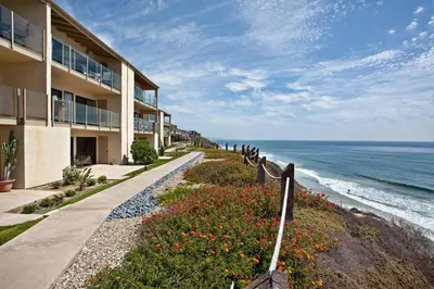 a building next to the ocean with a sidewalk and flowers at Serenity By The Sea - SBTC202 in Solana Beach