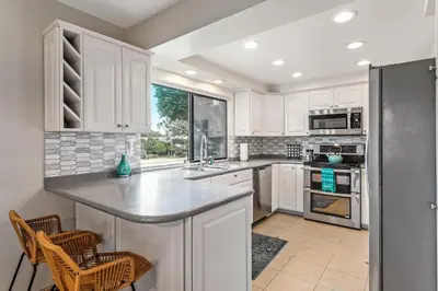 a kitchen with white cabinets and a stainless steel refrigerator at Drift Away - DMBC884 in Solana Beach